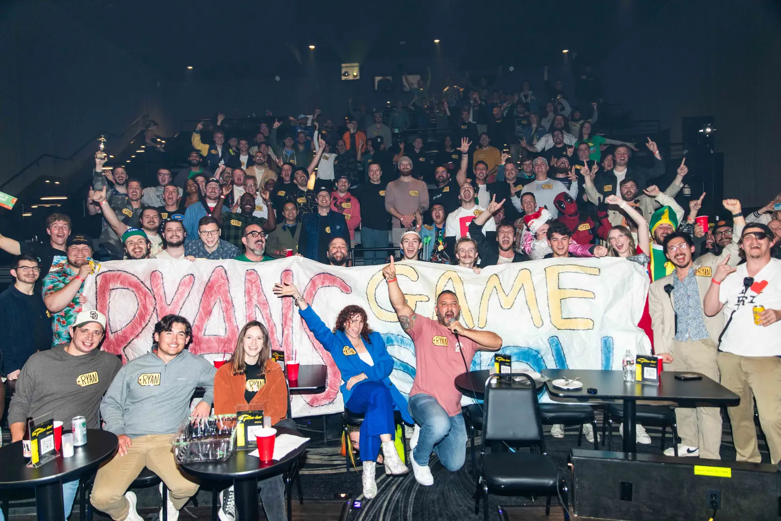 A packed theater of Ryans cheering behind a hand-painted Ryan Game Show banner